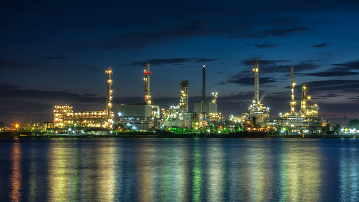 Illuminated oil refinery at dusk with lights reflecting across calm water