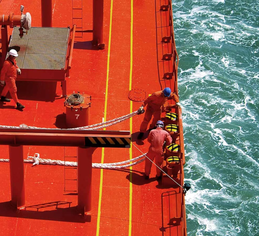 Crew members working on the deck of an ocean-going vessel alongside turquoise water